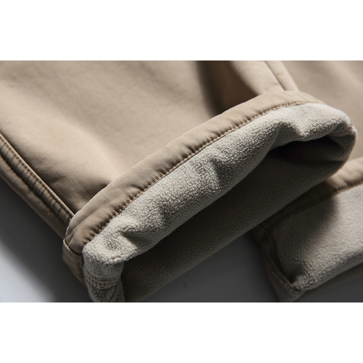 Close-up of a turned-up beige trouser cuff showing its light fleece lining and stitched outer fabric.