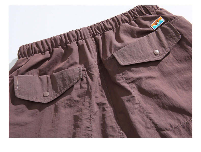 Flat lay of the upper front of brown shorts with an elastic waistband and two buttoned flap pockets.