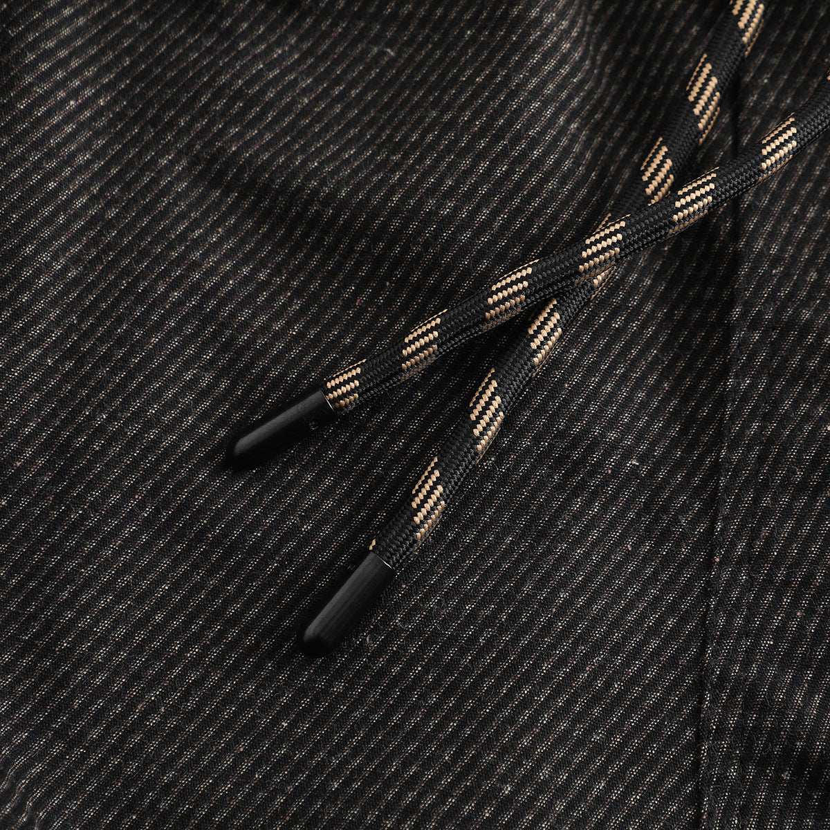 Close-up of black drawstrings with tan accents and plastic tips against dark striped pants.