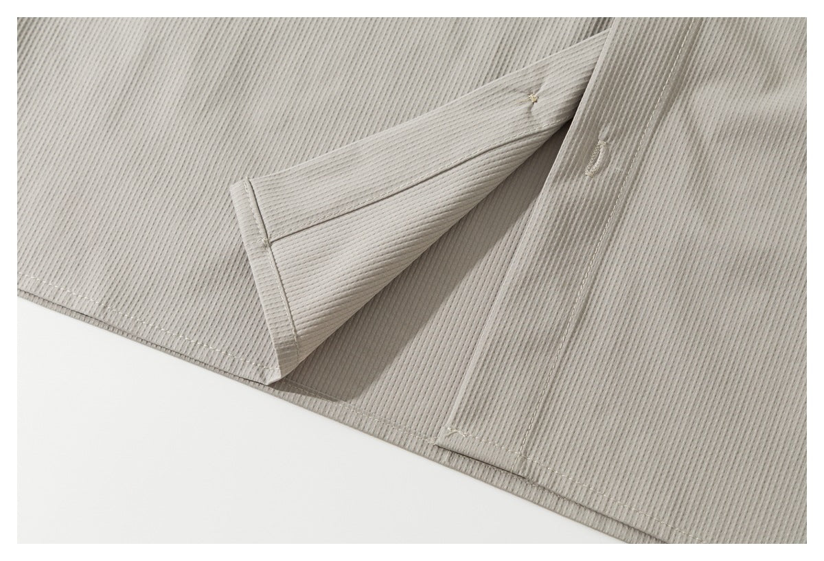 Close-up of a folded section of the light taupe shirt showing ribbed fabric, seams, and a buttonhole.