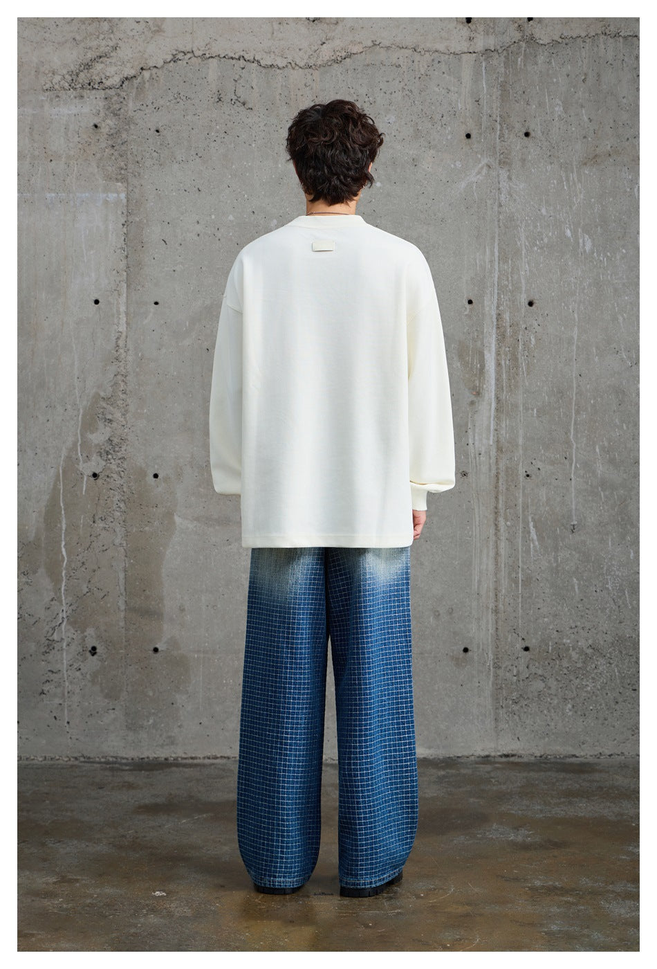 Rear view of a model in an oversized ivory sweatshirt with a small blank patch below the collar and wide-leg checked