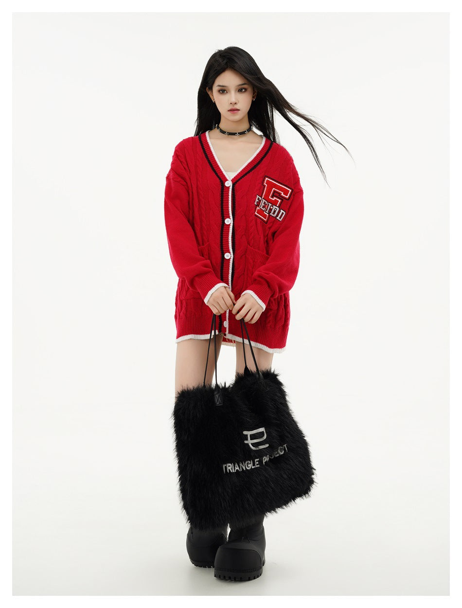 Model wearing an oversized red cable-knit cardigan with striped trim and a chest patch, carrying a black furry tote.
