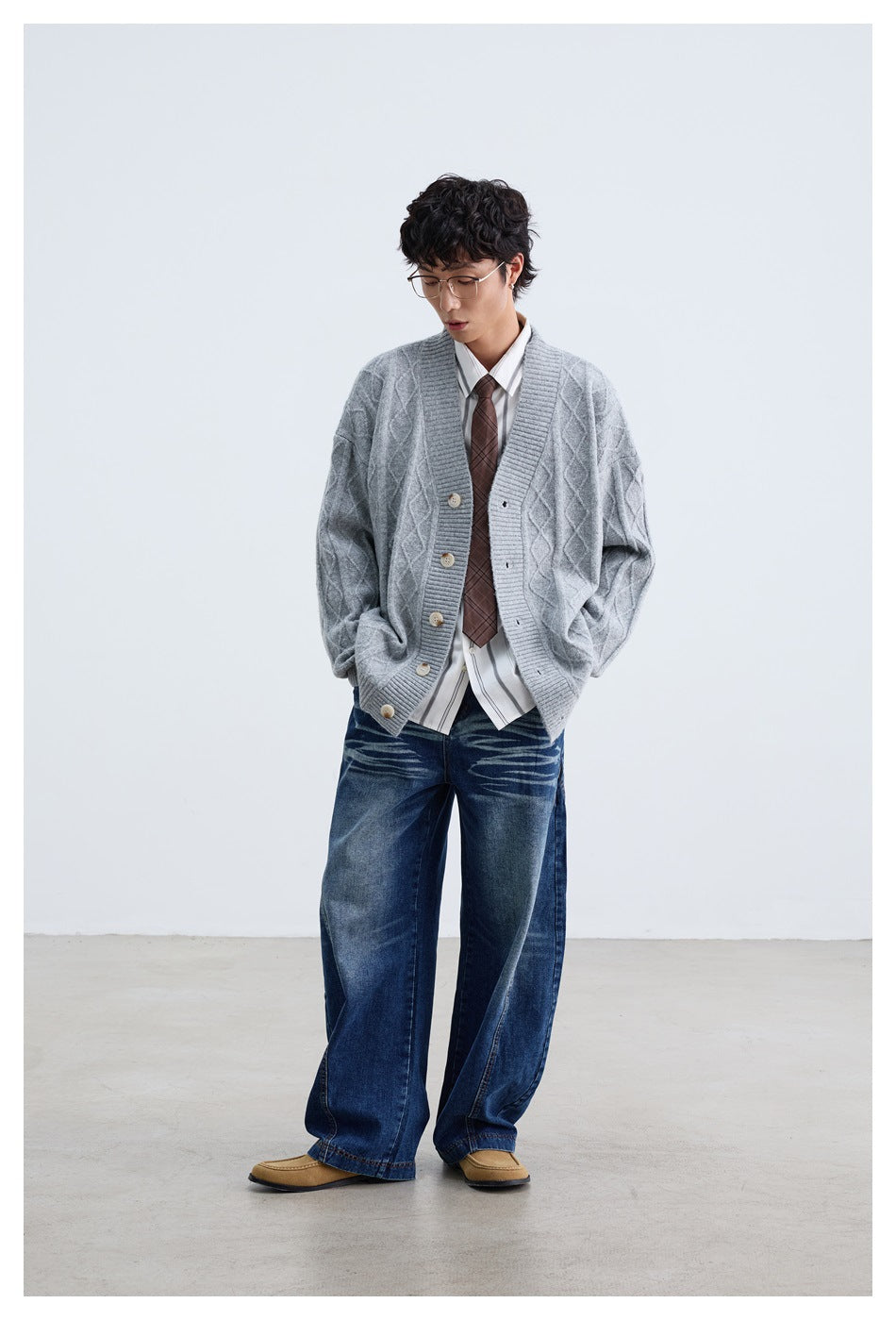 Full-length model wearing a light gray cable-knit cardigan with a striped shirt, tie, and wide-leg jeans.