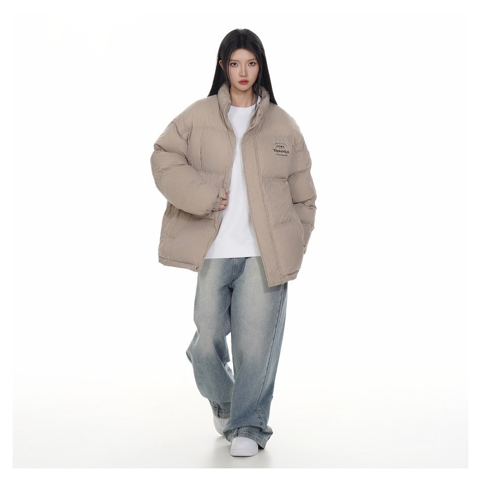 Full-length front view of a model wearing an open taupe puffer jacket with a white top and blue jeans.