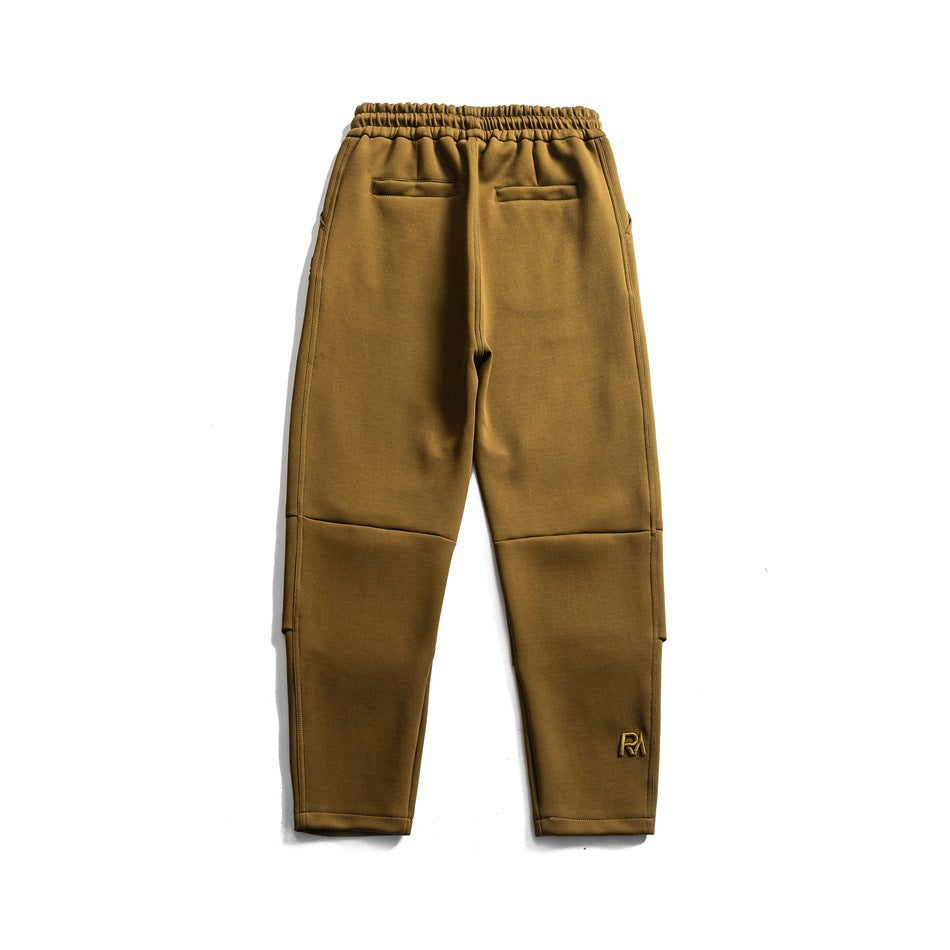 Back view of green olive-brown sweatpants with two welt pockets, elastic waist and small logo near the hem