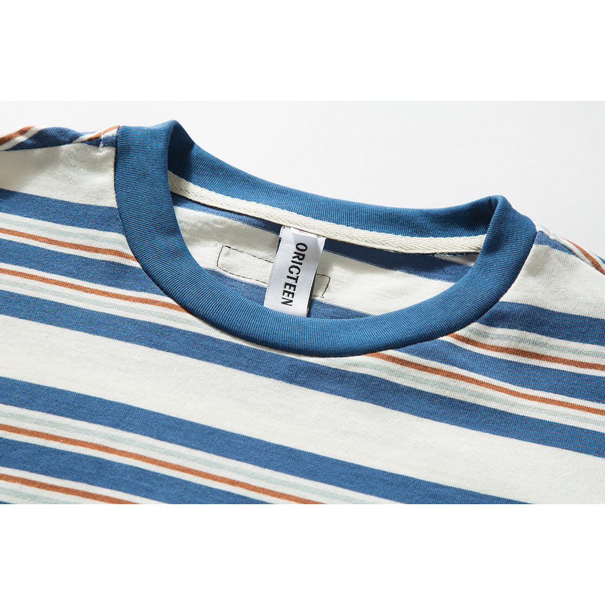Close-up of a cream T-shirt with blue, rust, and pale green stripes and a blue ribbed crew neck.