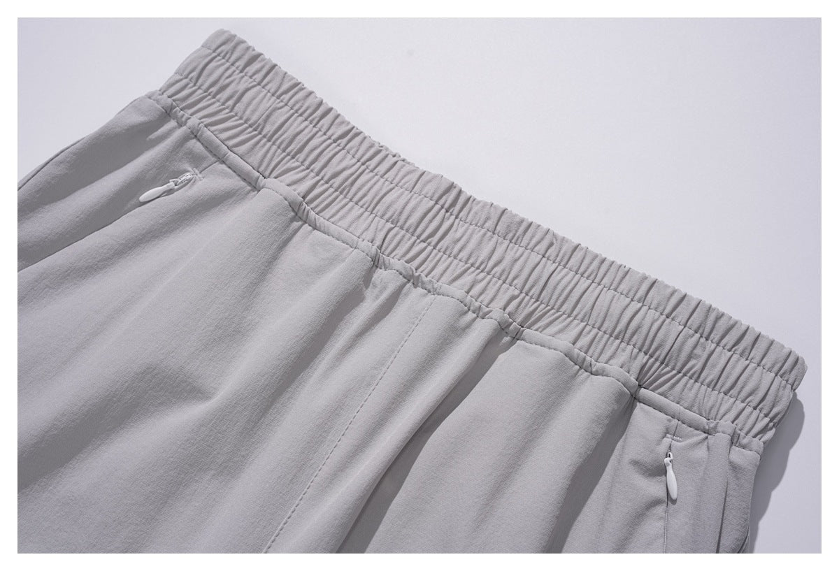 Close-up of light gray pants showing the gathered elastic waistband and zippered side pockets.