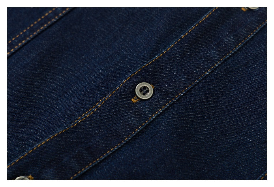 Close-up of a button on the dark indigo denim shirt, framed by contrast-stitched placket seams.