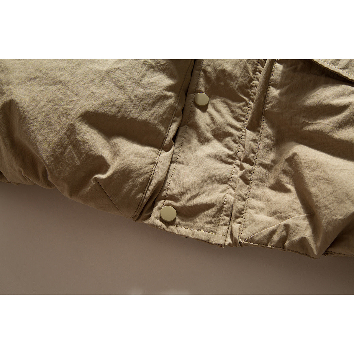 Close-up of the lower front of a tan jacket with two snap buttons and stitched seams.