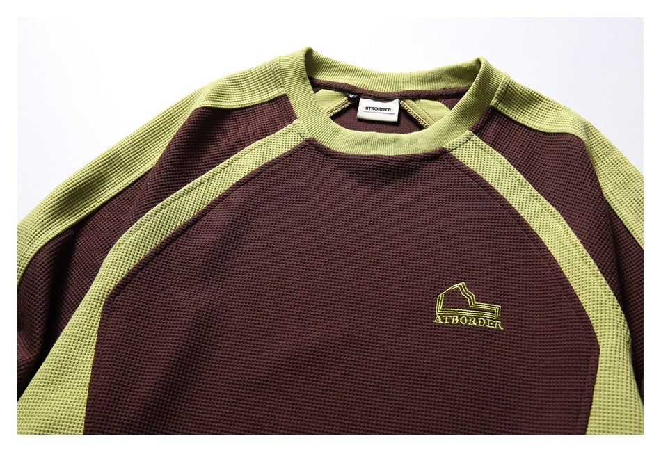 Close-up of the burgundy and lime-green top’s textured fabric, neckline, label, and embroidered chest emblem.