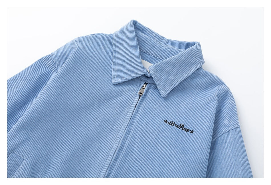 Close view of a light blue corduroy jacket’s pointed collar, front zipper and small black chest embroidery.
