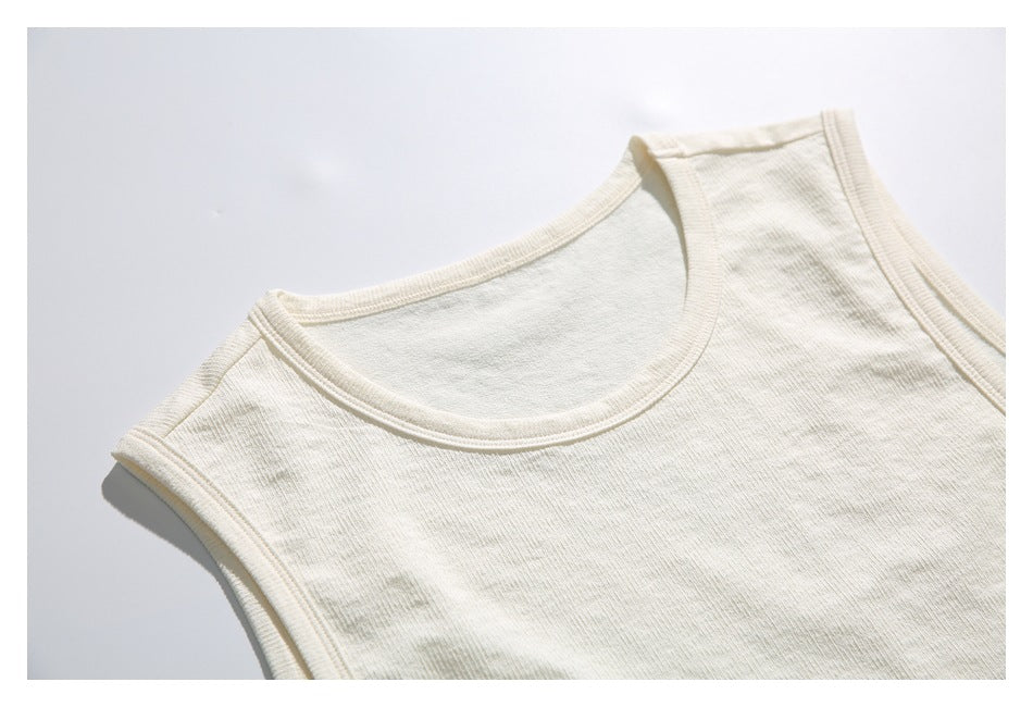Close view of an ivory sleeveless top laid flat, showing its scoop neckline and bound armholes.