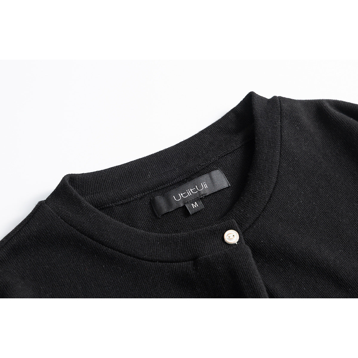 Close-up of a black top's round neckline, small button, and sewn-in neck label.
