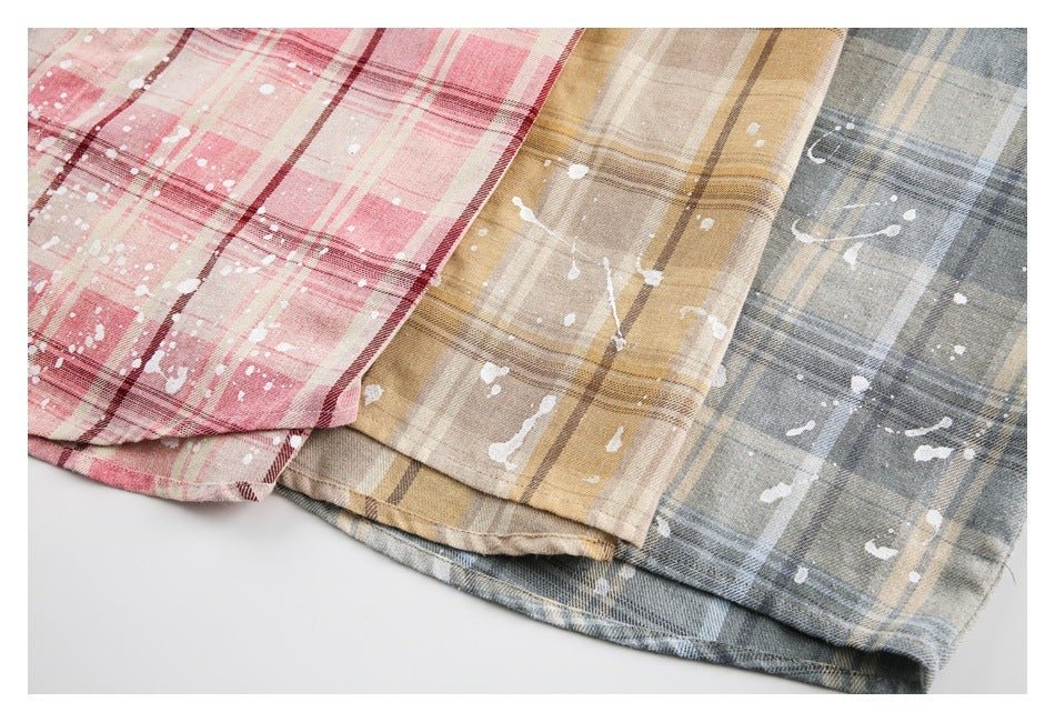 Close-up of the hems of pink, tan, and gray-blue plaid shirts with white paint-splatter details.