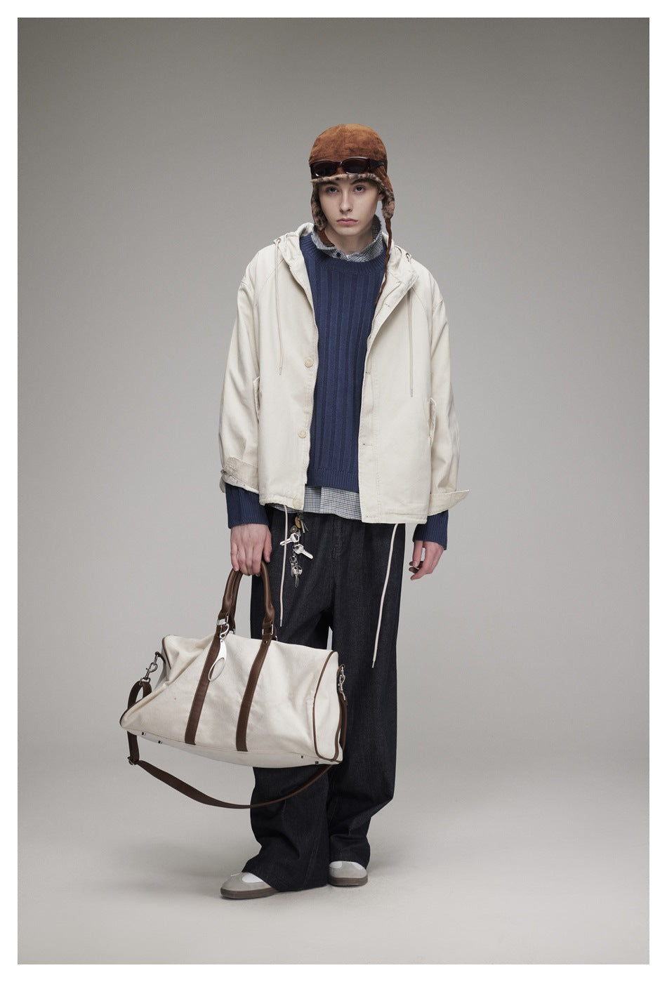 Full-length model wearing an off-white hooded jacket, navy sweater, dark wide-leg trousers, and a brown fur-trimmed hat.