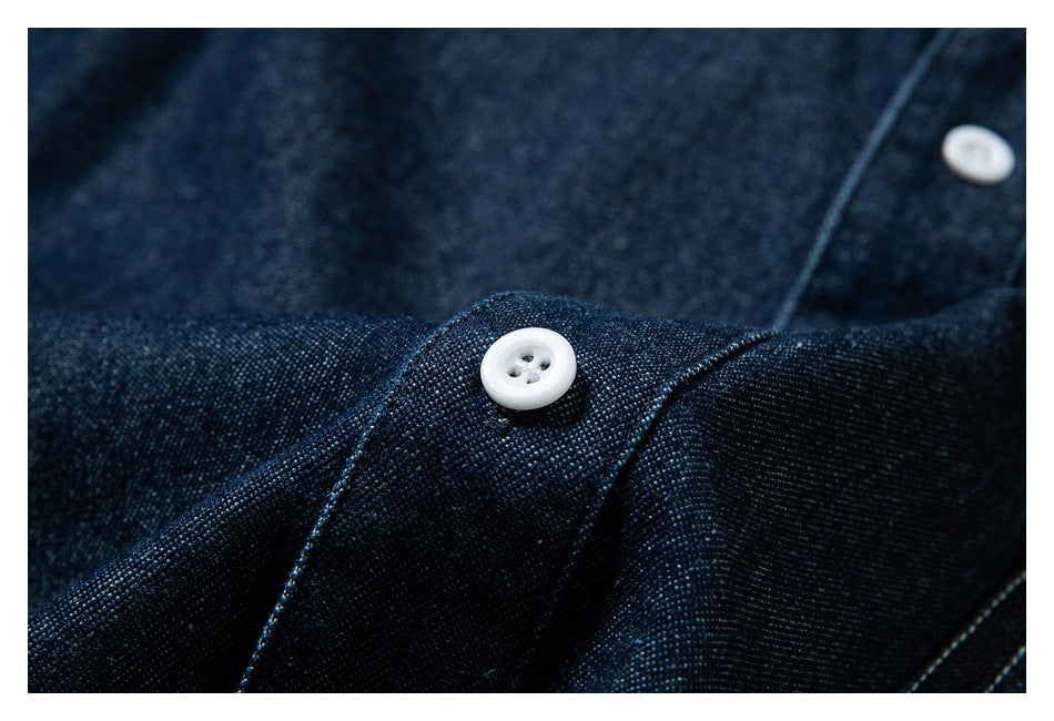 Macro view of a white button and stitching on dark indigo shirt fabric.