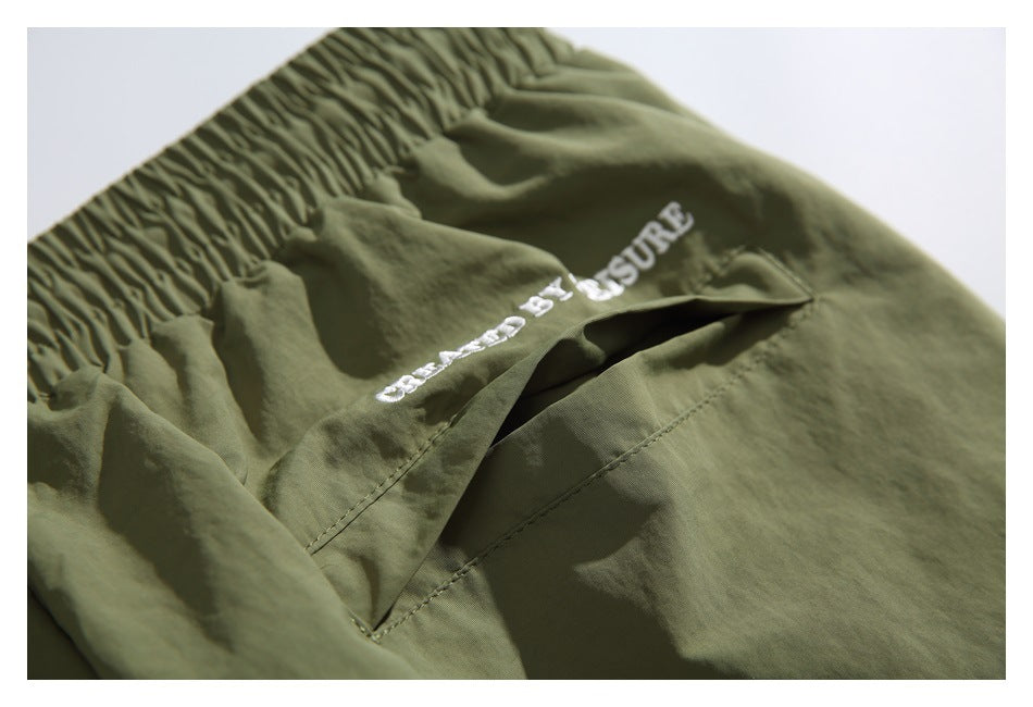 Close-up of an open rear pocket and white embroidery on olive-green shorts.