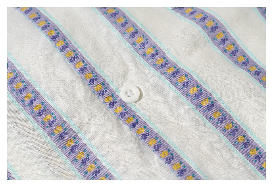 Close-up of a white button on ivory fabric with lavender floral stripes and turquoise borders.
