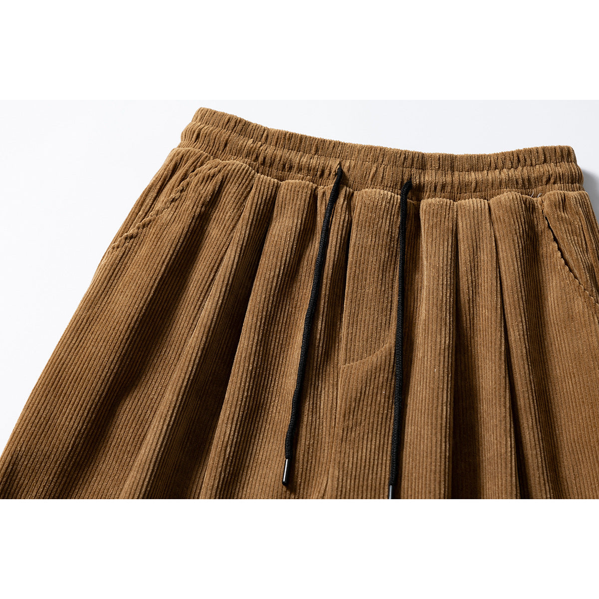 Close-up of brown corduroy pants with a gathered elastic waistband, pleats, and black drawstrings.