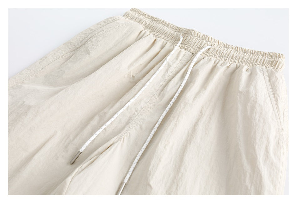 Front view of cream drawstring pants laid flat, with an elastic waistband and angled pockets.