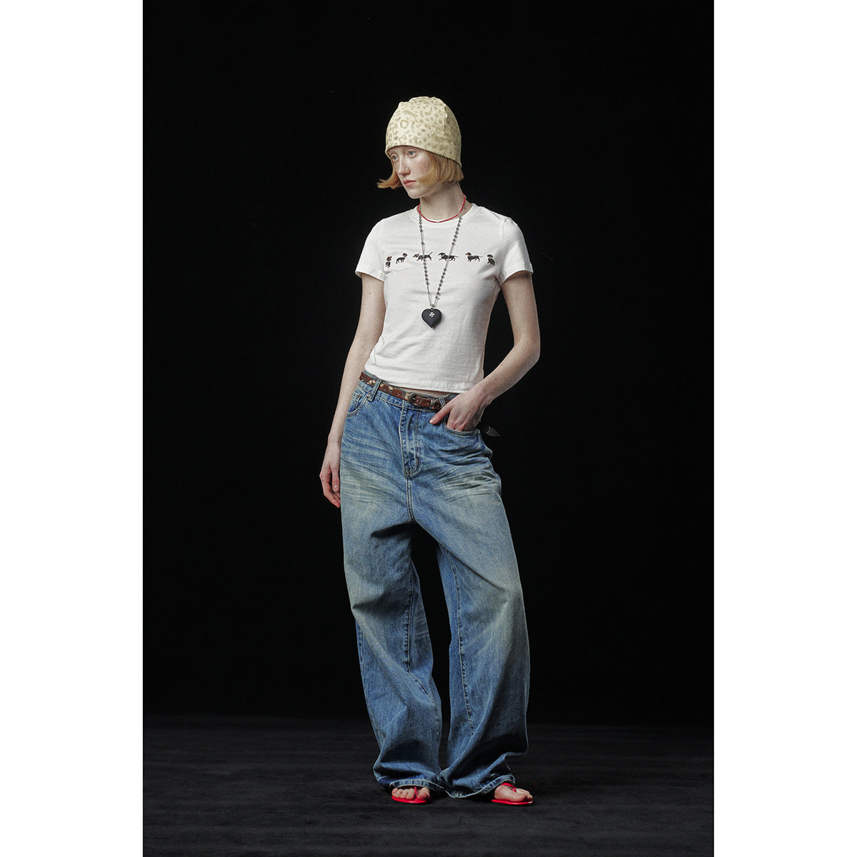 Model wearing a white dachshund-print T-shirt with loose blue jeans and a beige patterned beanie.