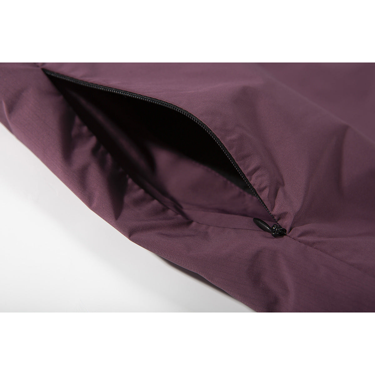 Close-up of a dark plum garment with a curved black zipper pocket.