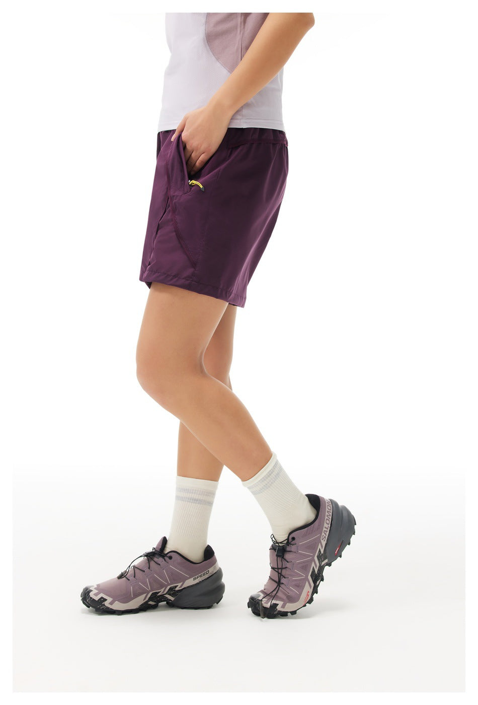Side view of a model wearing plum athletic shorts, showing the pocket and yellow zipper pull.