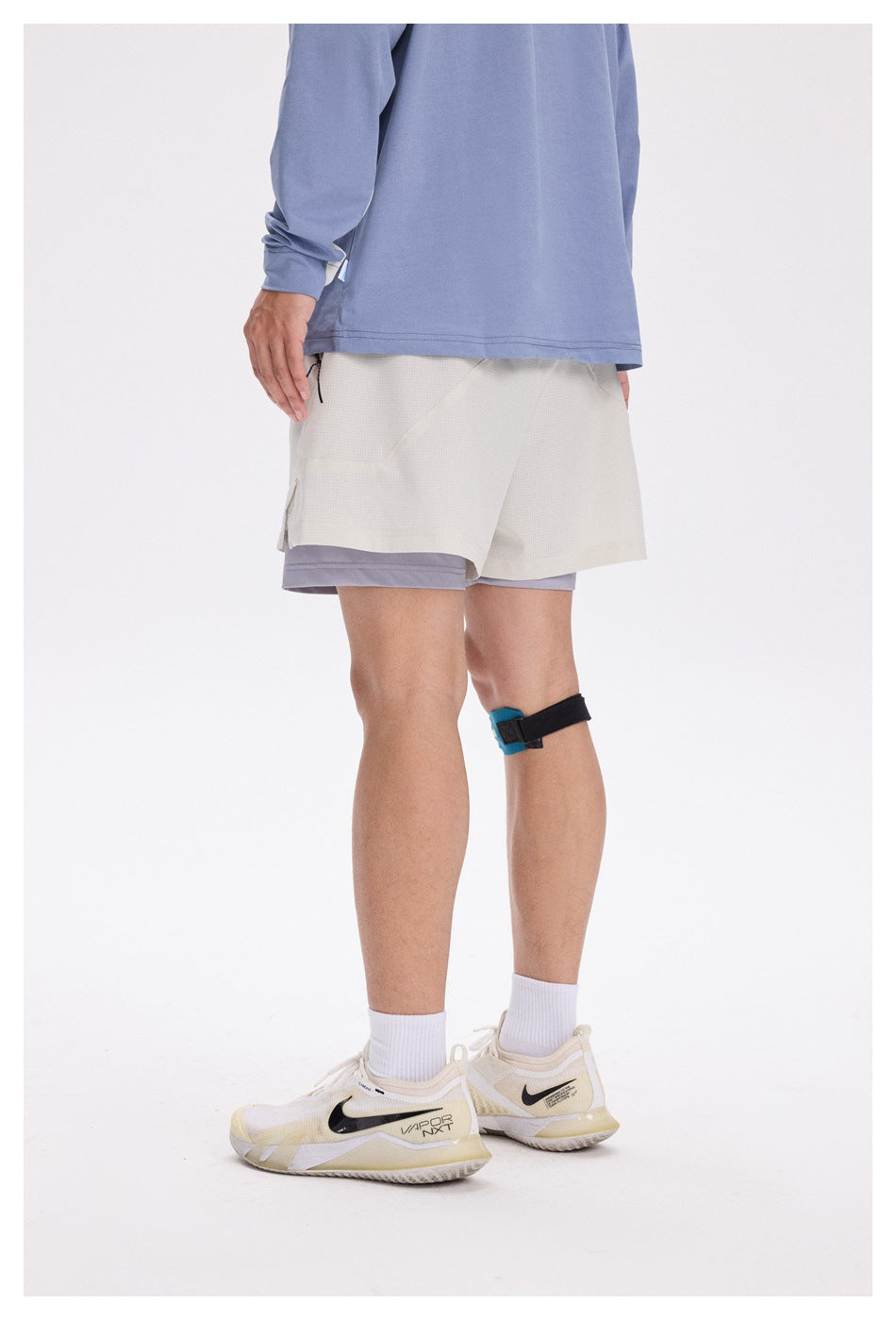 Rear view of a model wearing light gray shorts over lavender compression shorts.