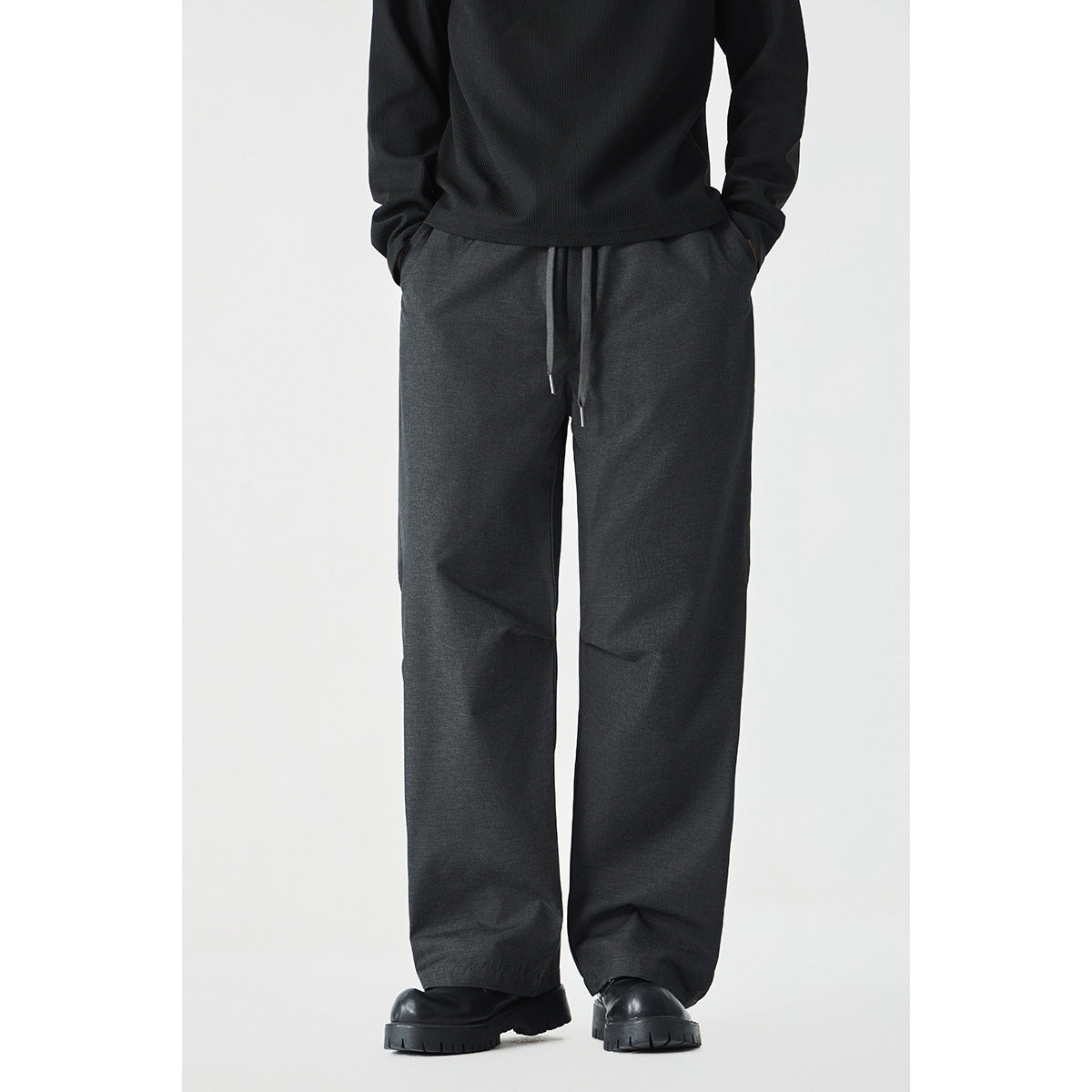 Cropped model wearing wide-leg charcoal drawstring pants with a black top and chunky black shoes.