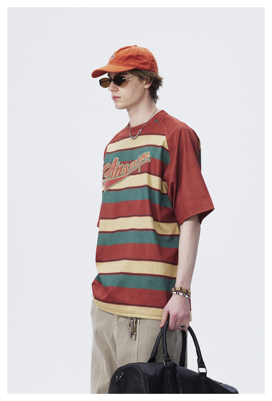 Side-angle view of a model wearing a rust, teal and cream striped graphic T-shirt with beige trousers.