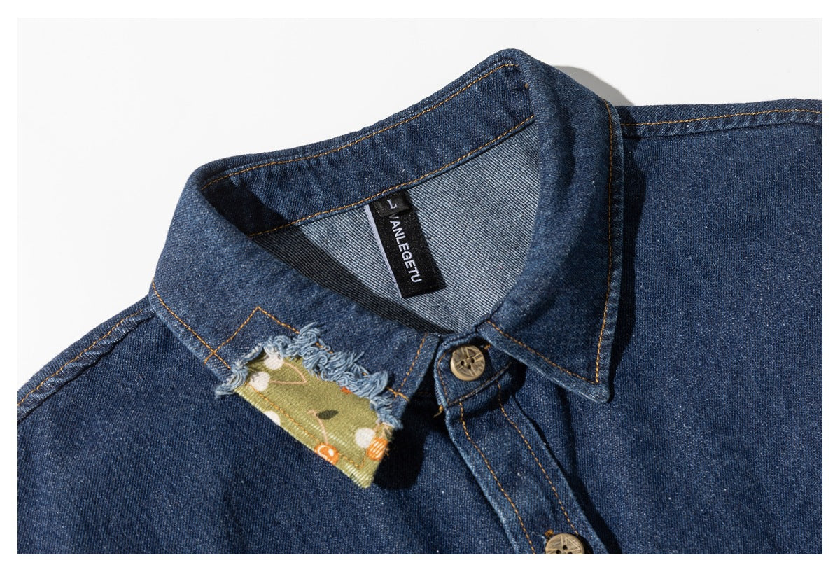 Close-up of a dark blue denim shirt collar with a frayed green floral patch and a visible black neck label.