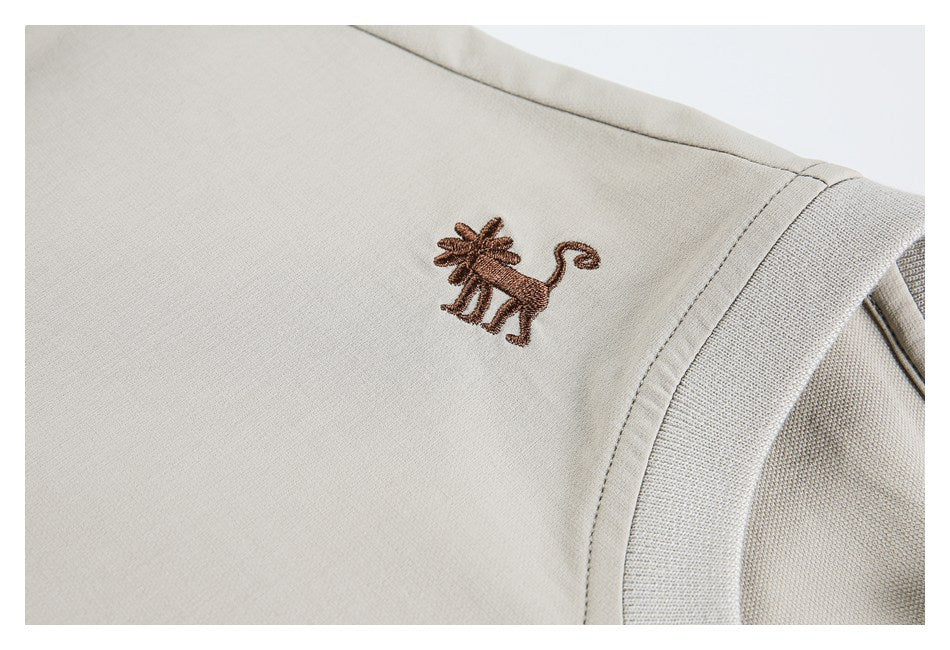 Close-up of a small brown embroidered animal on beige fabric beside the ribbed collar seam.