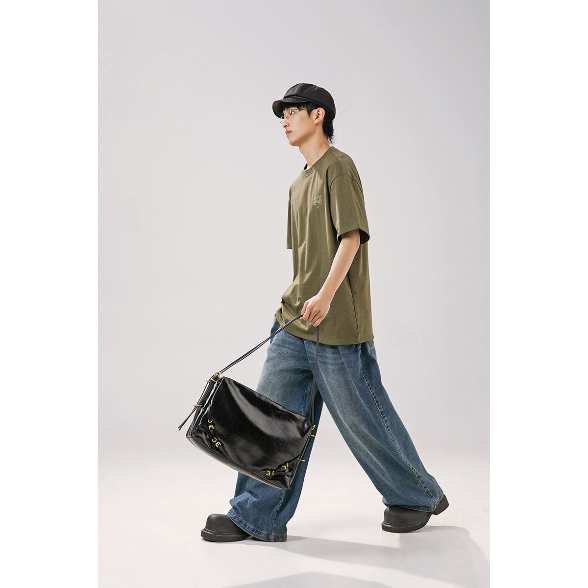 Model in profile wearing an oversized olive green T-shirt with a small chest graphic and wide-leg blue jeans.