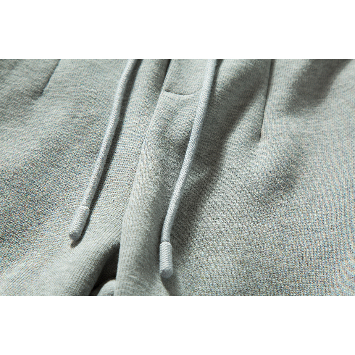 Close-up of light gray sweatpants showing two matching drawstrings and the textured fabric.