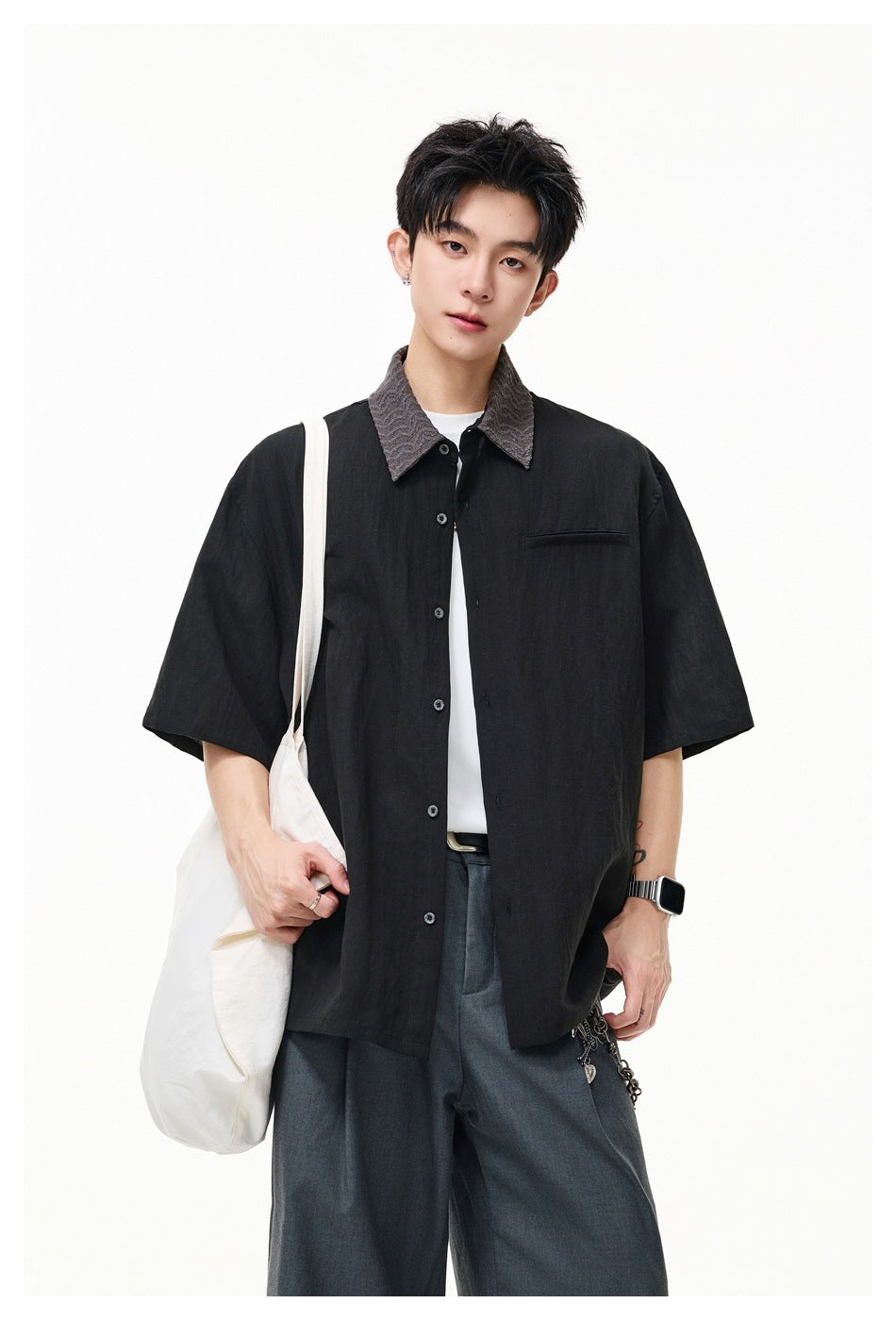 Front view of a model wearing a black short-sleeve button-up shirt with a textured gray collar and chest pocket.