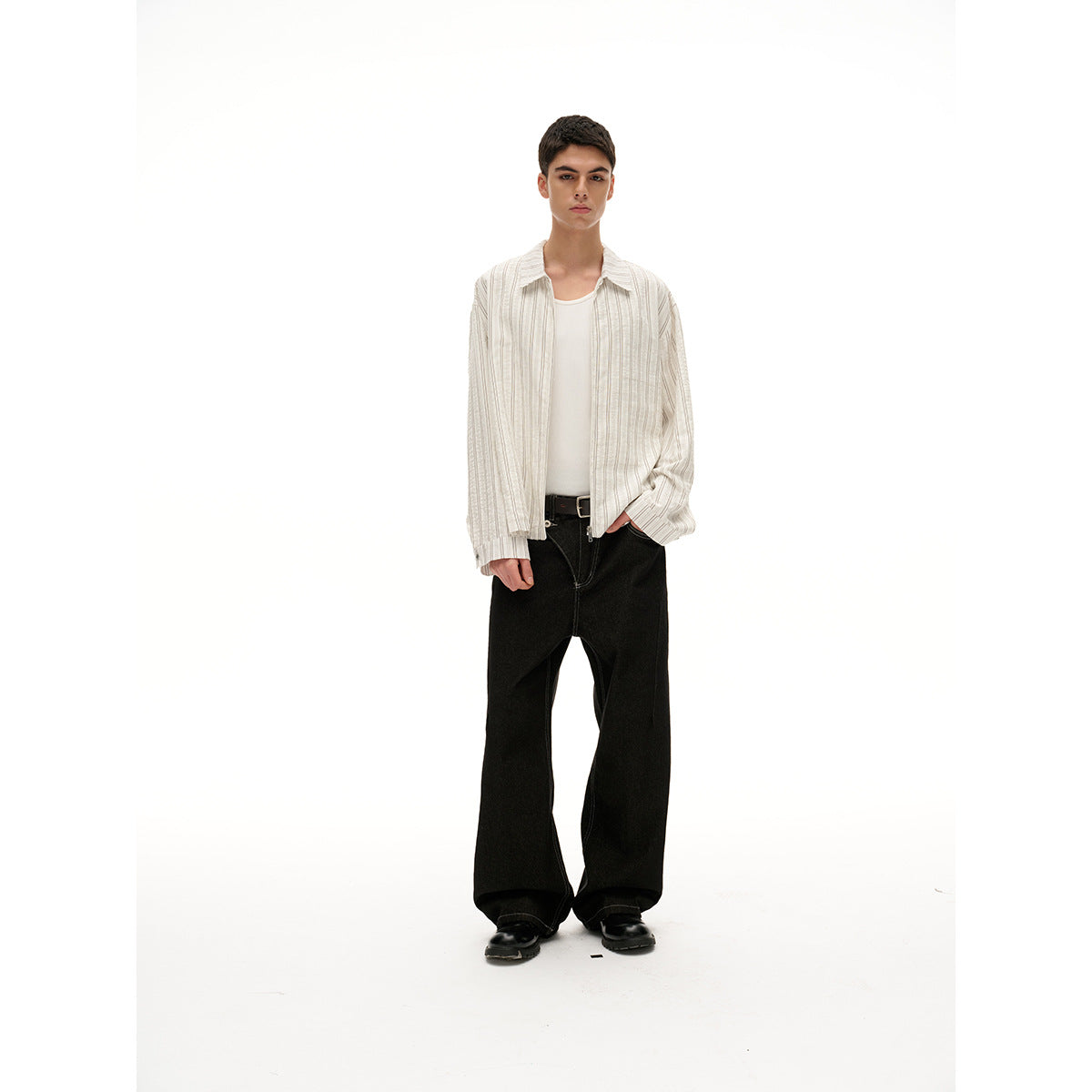 Front view of a model wearing an open cream shirt with fine vertical stripes over a white tank and black trousers.