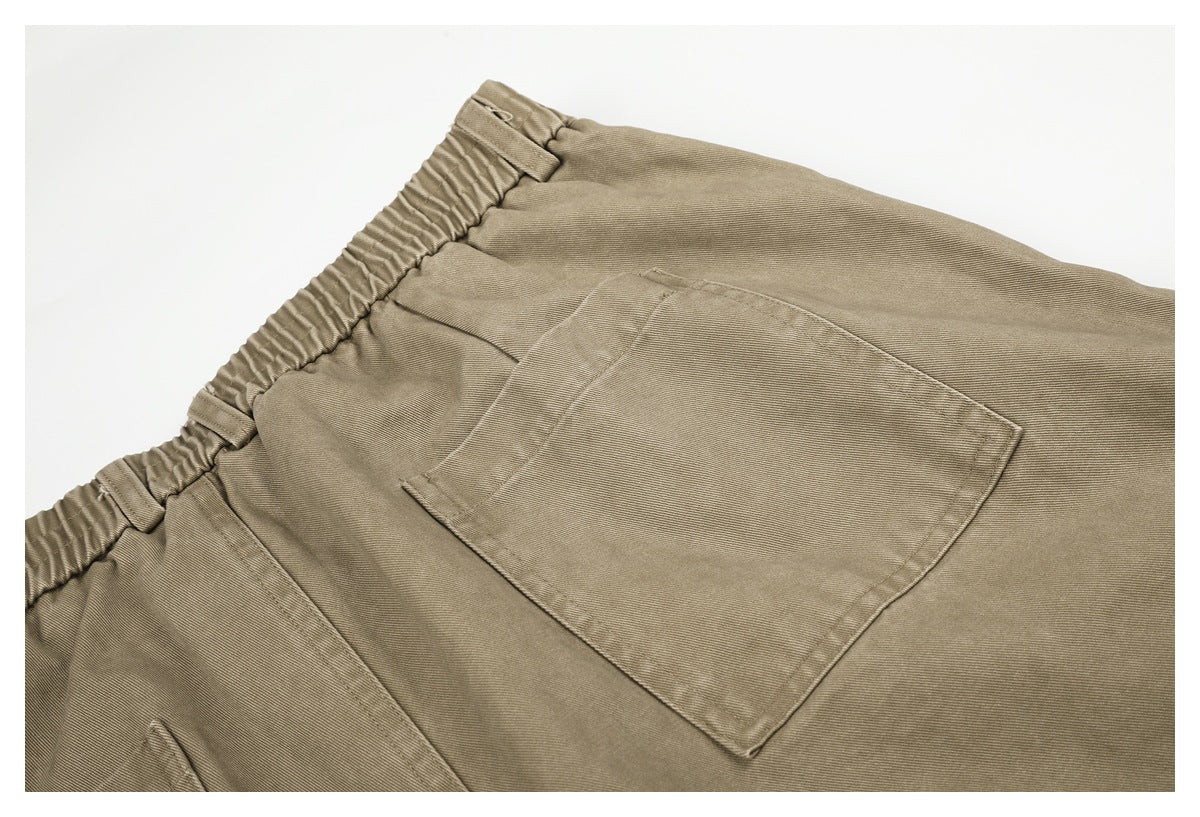 Close-up of taupe-brown trousers showing the elastic waistband and a large patch pocket.