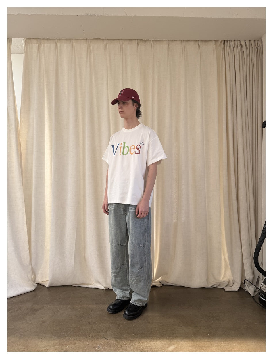 Side-angled view of a model in light blue wide-leg jeans with a white graphic T-shirt, red cap and black shoes