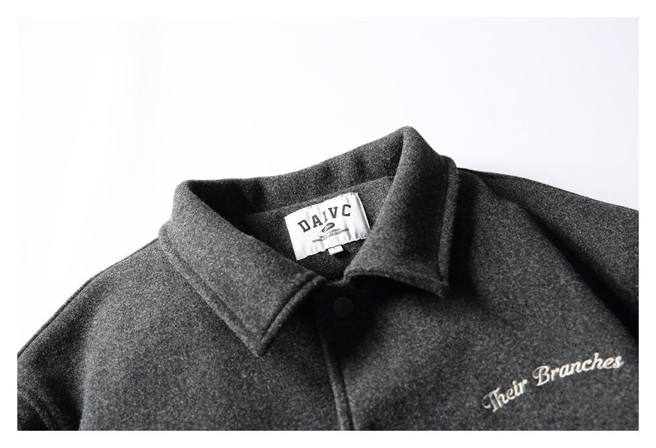 Close-up of a charcoal gray jacket collar, sewn neck label, black snap, and cream chest embroidery.