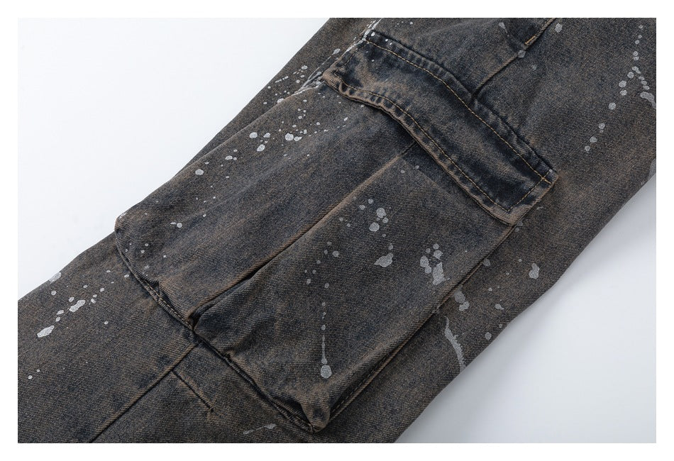 Close-up of a flap cargo pocket on dark washed denim, scattered with pale paint splatters.