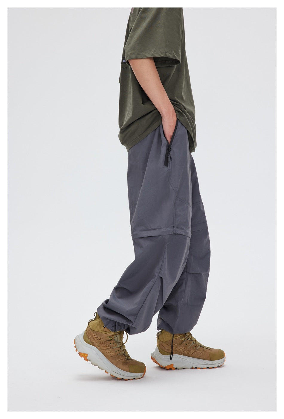 Side view of a model wearing slate-gray convertible pants with a zip pocket and adjustable ankle hems.
