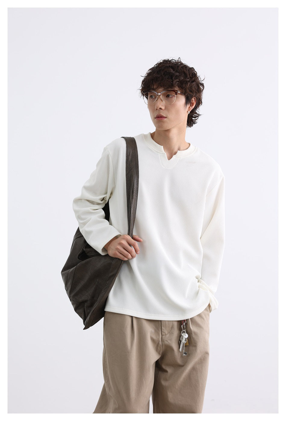 Model wearing an ivory ribbed notched-neck top with beige trousers and carrying a dark shoulder bag.