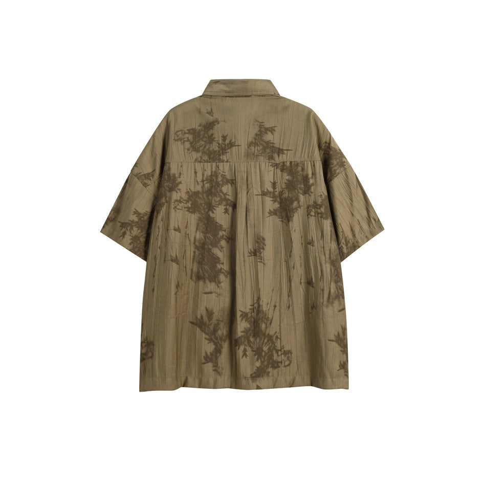 Back view of a loose olive-brown short-sleeve collared shirt with a dark botanical pattern.