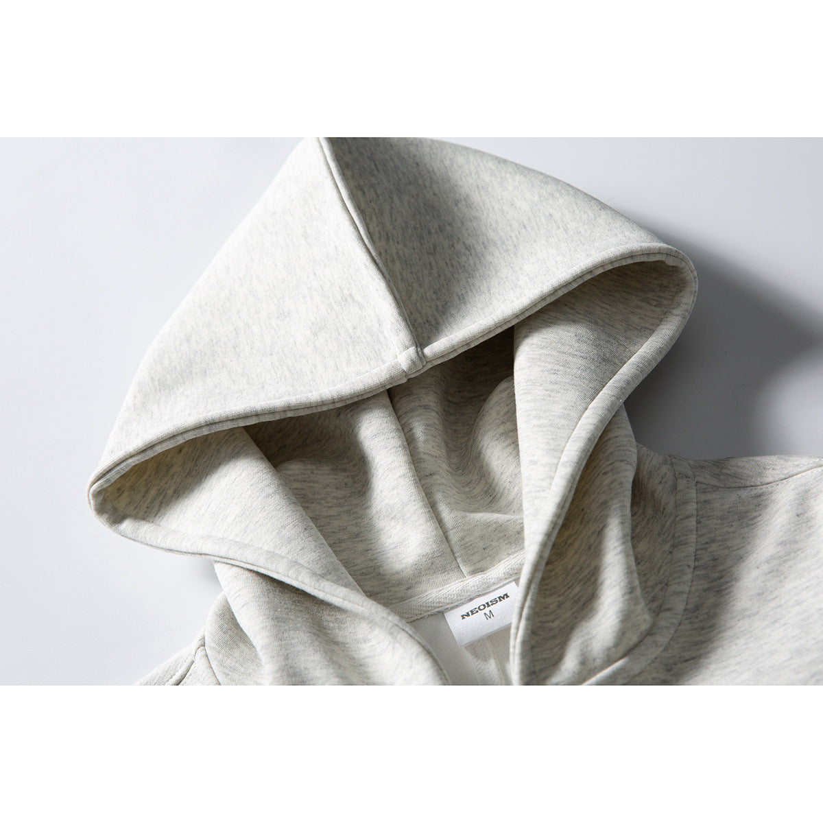 Close-up of a light gray heather hood on a zip-up sweatshirt, showing its seams and neck label.