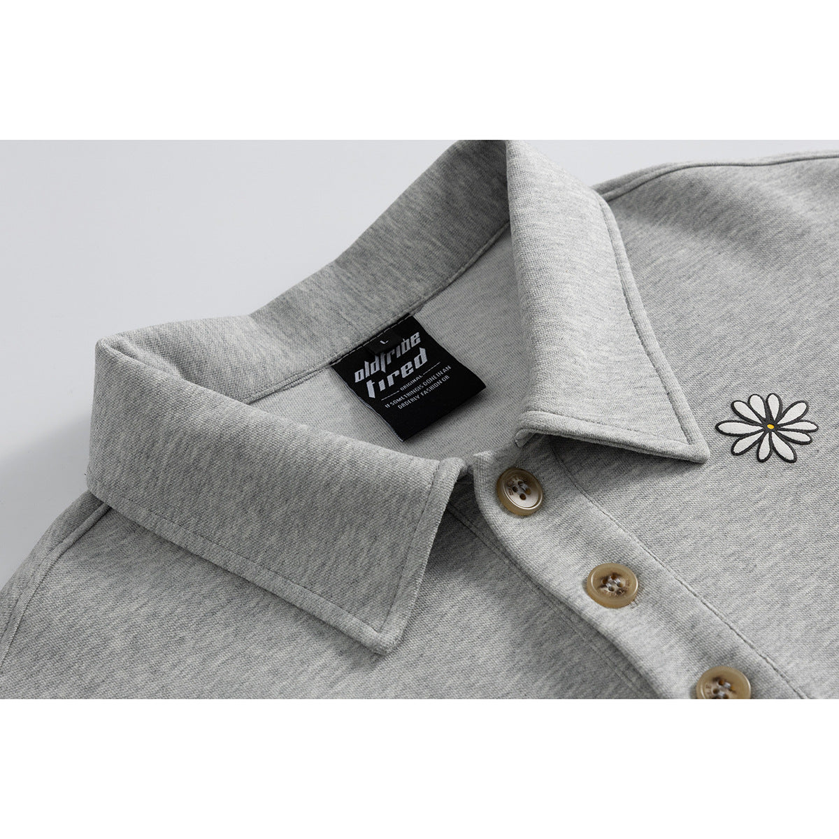 Close-up of a heather gray collared pullover showing its button placket, daisy embroidery, and sewn neck label.