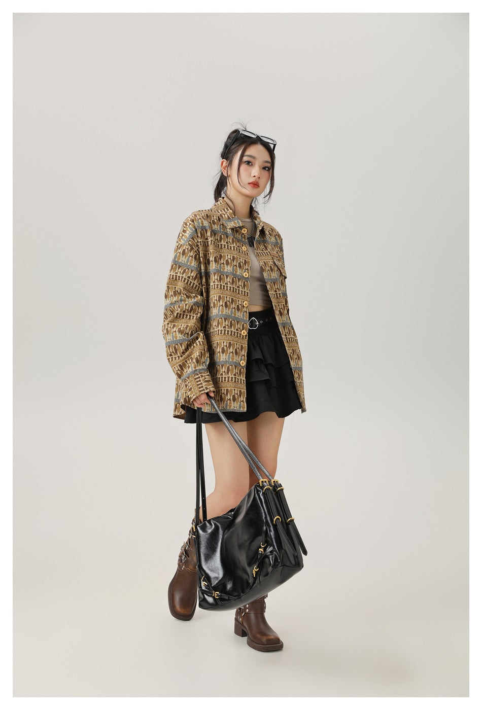 Full-length view of model wearing the brown patterned oversized shirt open with a black skirt, boots and large black bag