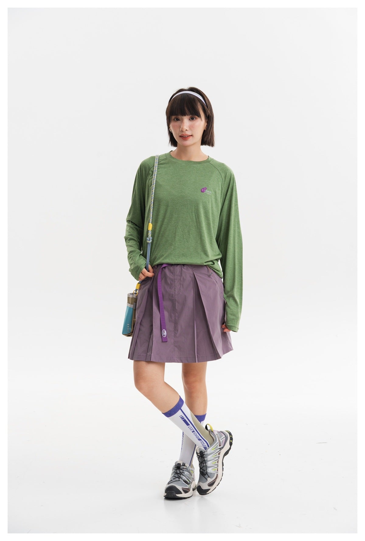 Model wearing a green long-sleeve shirt and lavender pleated skirt, posed at a slight angle.