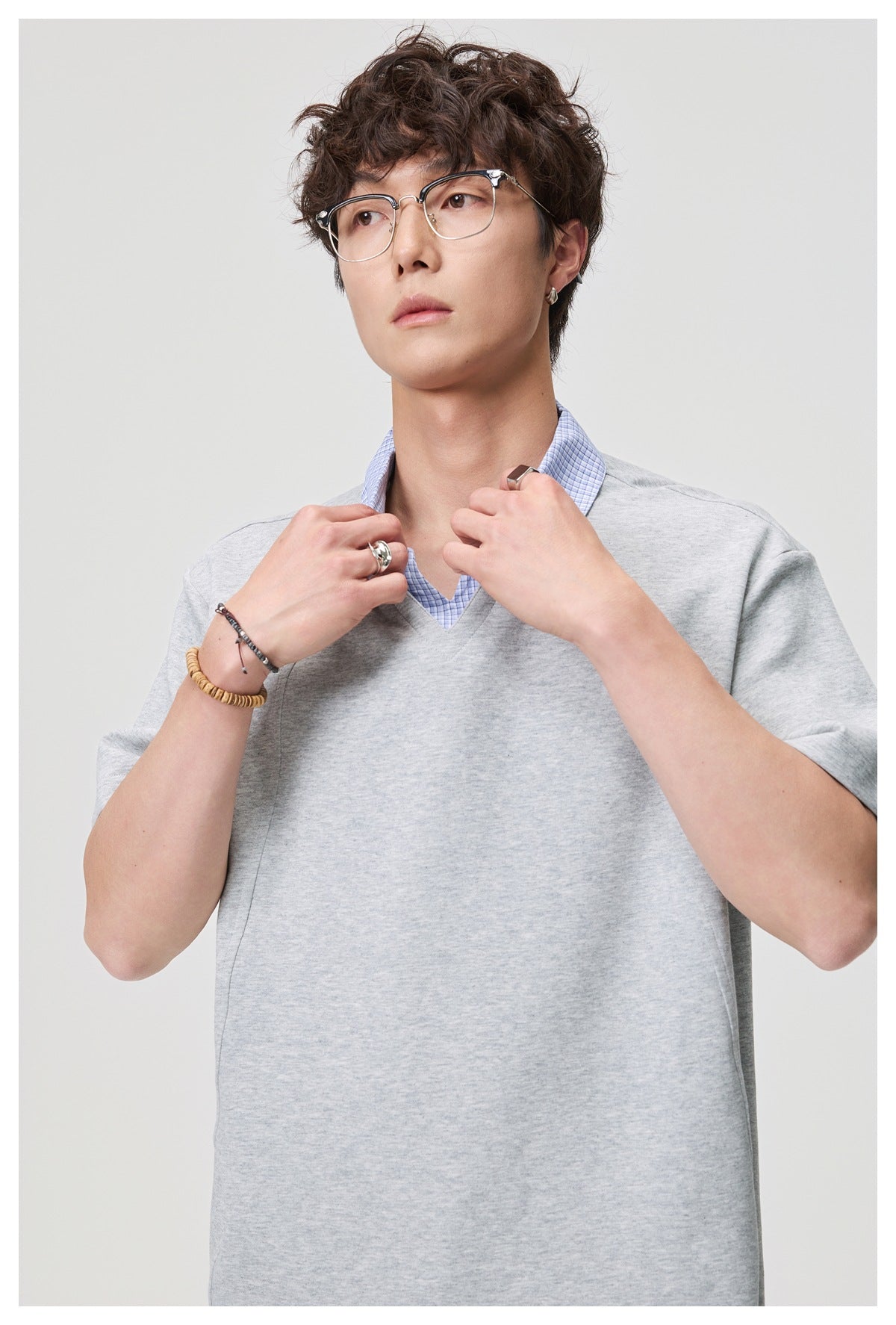 Close-up of man in gray top with blue check layered collar and V-neck, hands at collar