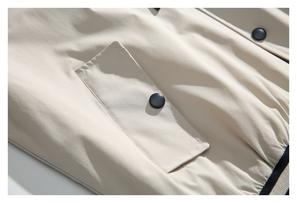 Close-up of an ivory jacket's rectangular flap pocket with a black snap button.
