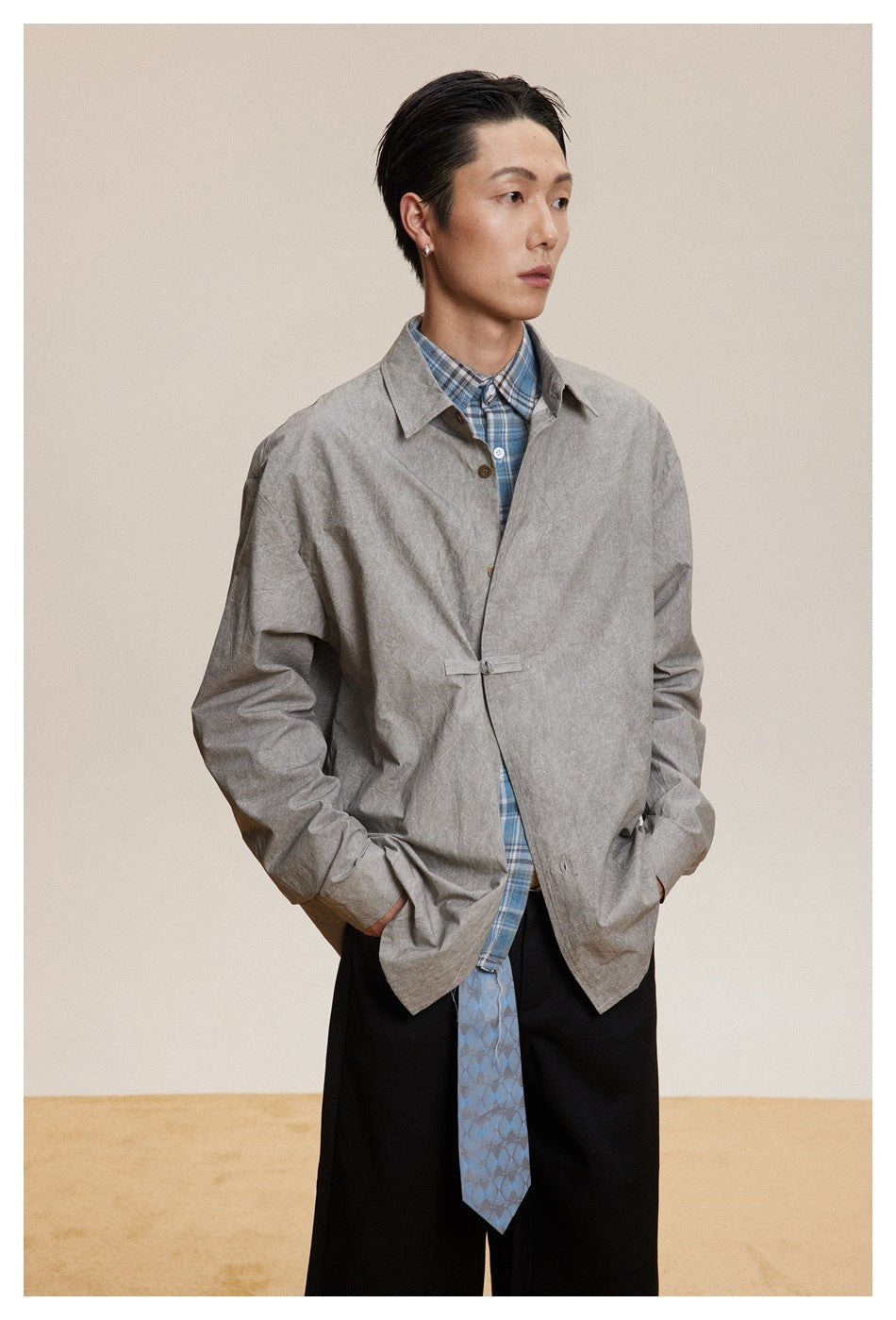 Model wearing a gray collared button-front jacket over a blue plaid shirt and black trousers.